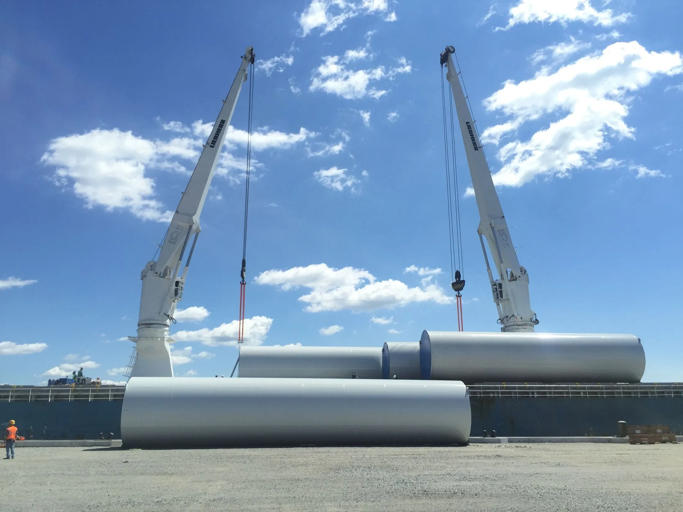 Ship cranes lifting large steel cylinders on a quay